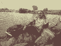 Me, posing for a photo prone on some rocks next to the sea; the image is dithered and small.